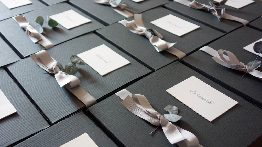 Schwarte Kartons mit Grußkarte "Glückwunsch", grauem Ripsband und Eukalyptus.