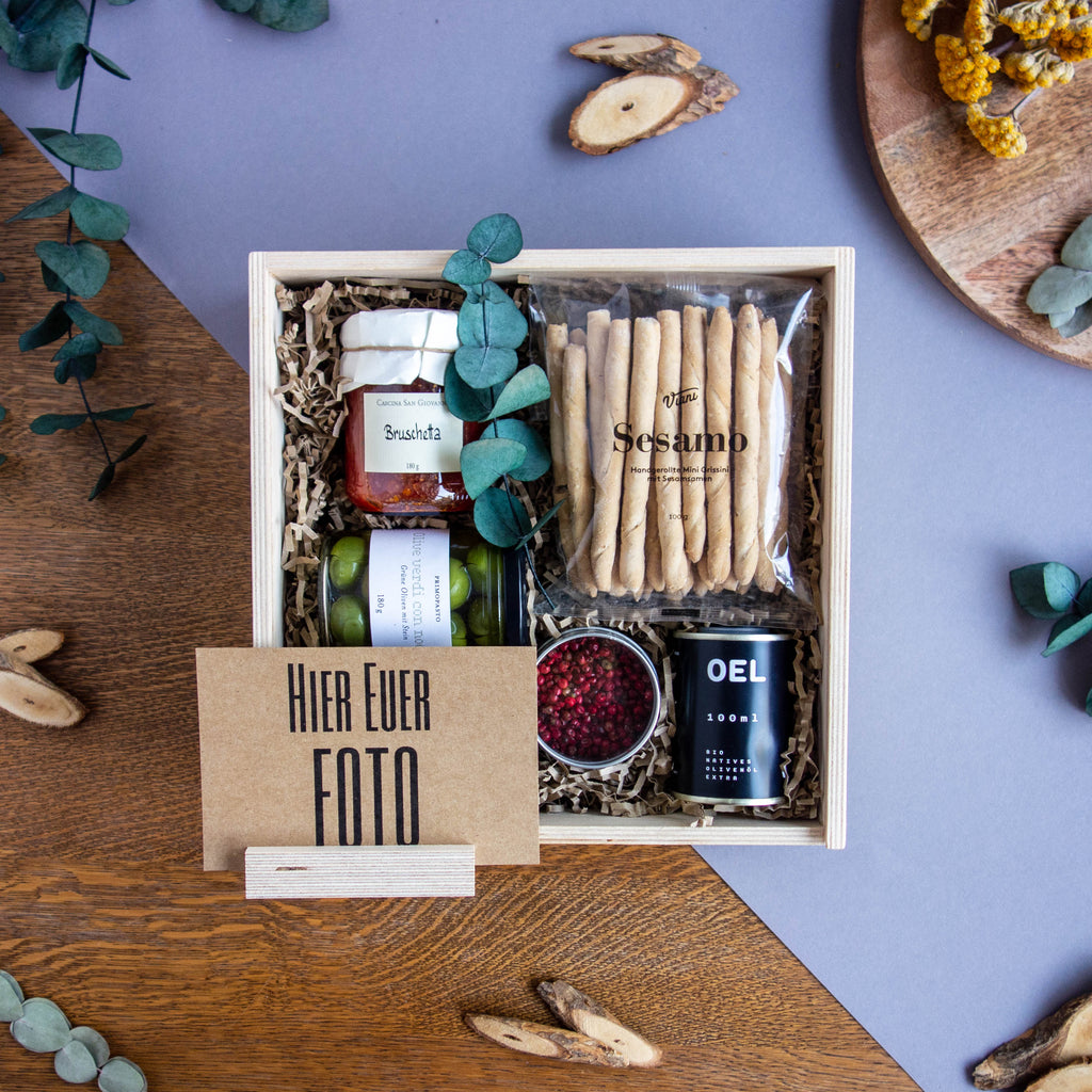 Holzbox gefüllt mit Bruschetta, grünen Oliven, Sesamstangen, Schinus Pfeffer und Olivenöl.